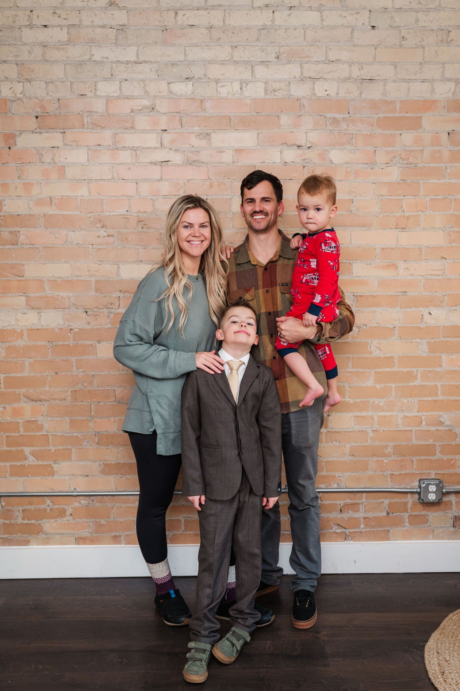 Family of four posing together against brick wall in casual and formal attire.