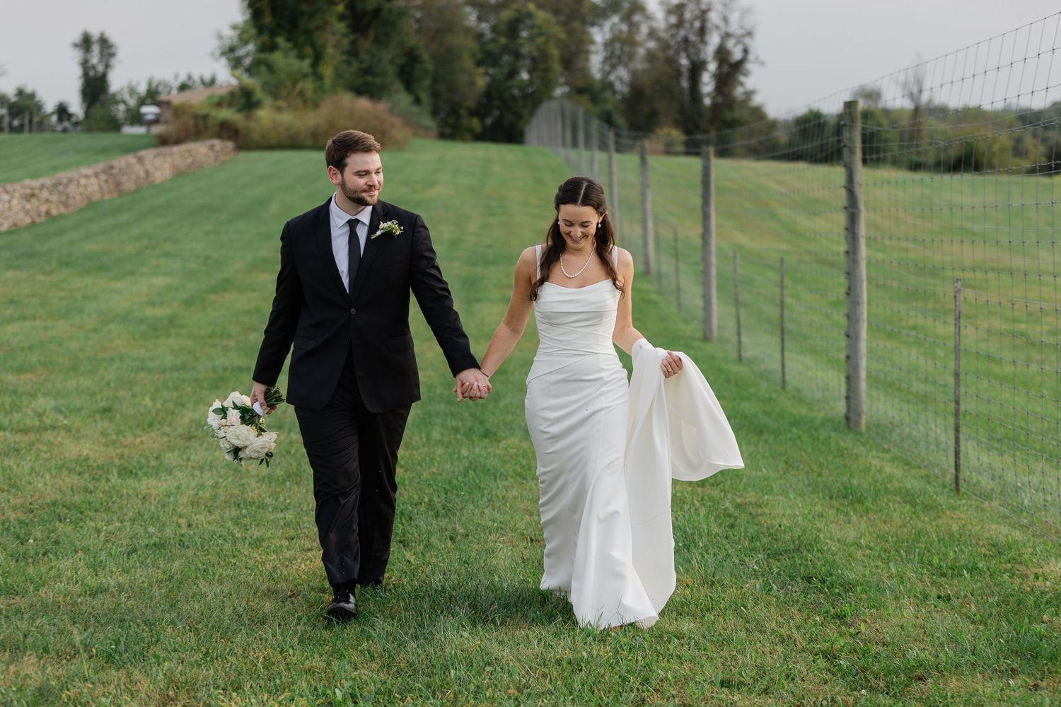 Newlyweds walking together on a wooden dock overlooking a serene lake.