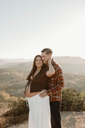 A romantic couple embraces on a hilltop during golden hour with rolling hills in the background.