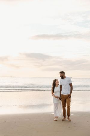 A couple walks along a peaceful beach at sunset, holding hands and enjoying the serene coastal atmosphere.