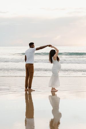 A couple dancing together on a reflective beach at sunset with ocean waves in the background.