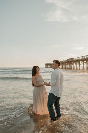 A couple dances in the ocean waves at sunset near a pier, creating romantic silhouettes against the golden sky.