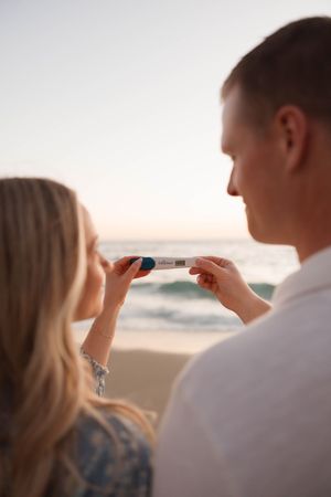Two people taking photos with their phones at sunset on a beach with ocean waves in the background.