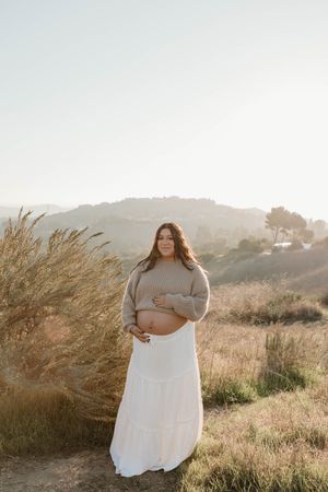 A series of outdoor maternity photos in golden sunlit fields with tall grass and mountains in the background.