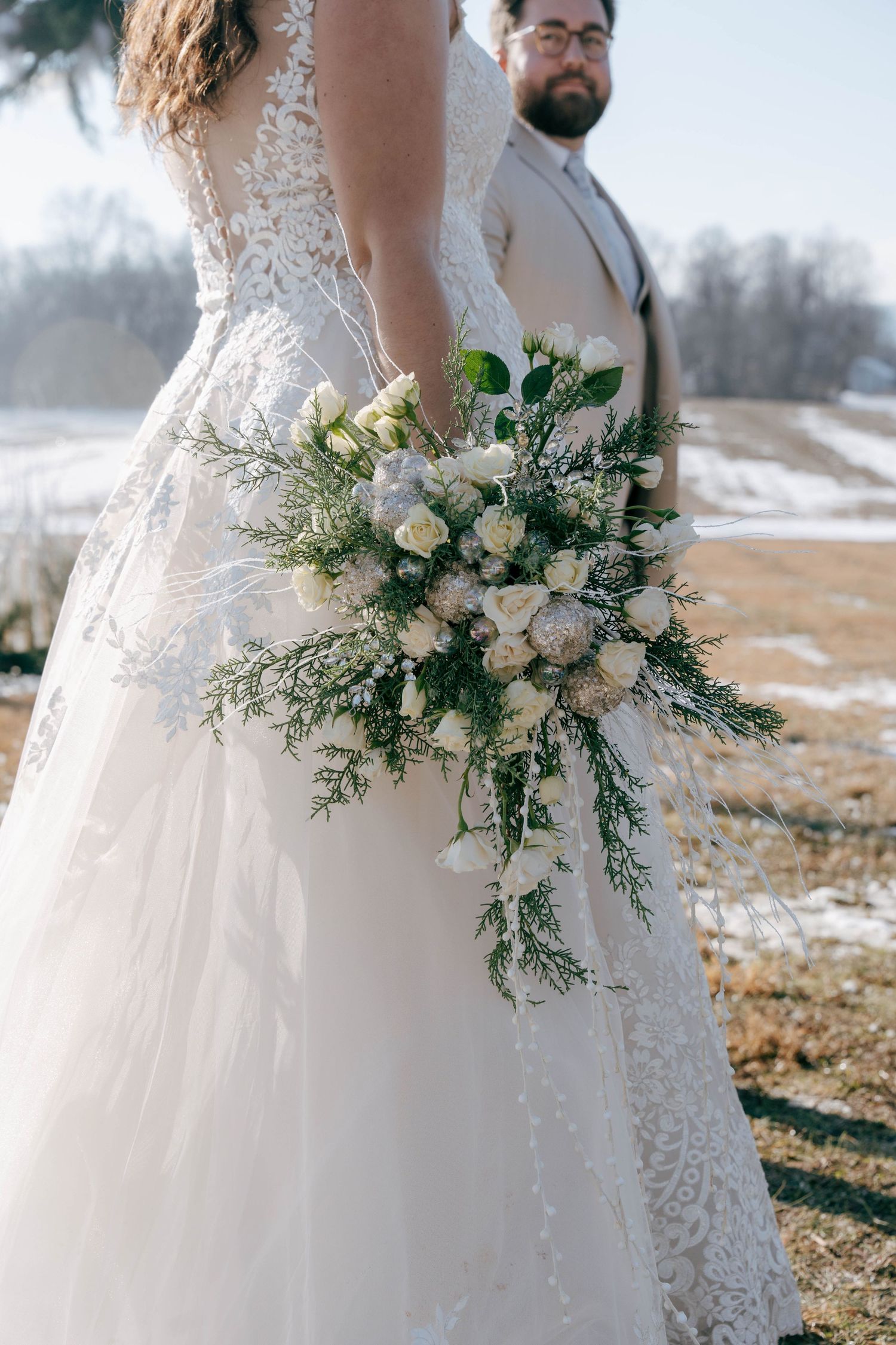 Elegant white bridal bouquet with roses and greenery against a snowy winter landscape background.