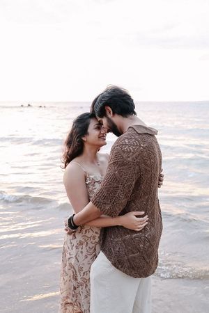 Couple shares tender moment on beach shoreline during golden hour photography session.
