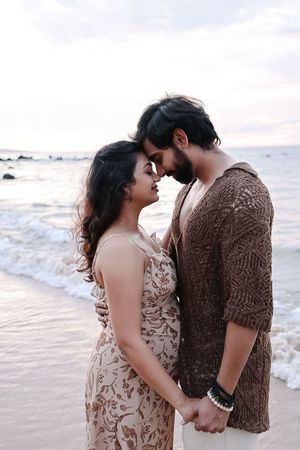 A romantic couple shares tender moments on a beach at sunset while waves crash behind them.