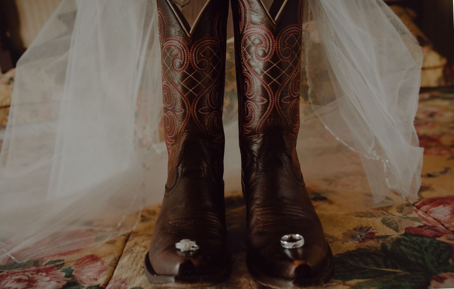 Detail shot of bride's cowboy boots, veil and wedding rings on vintage bedding in their hotel.