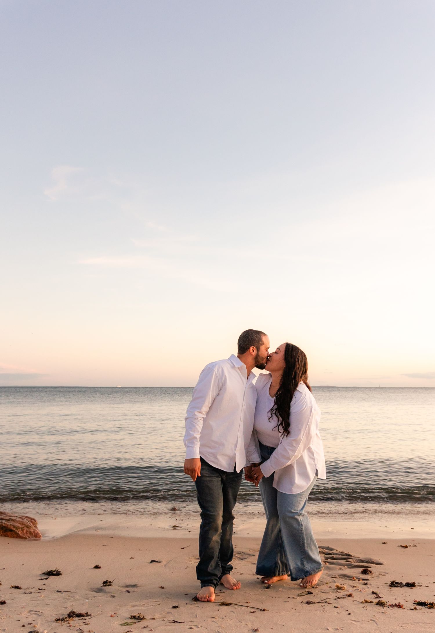 Romantic sunset beach scene with couple in white outfits sharing intimate moment.