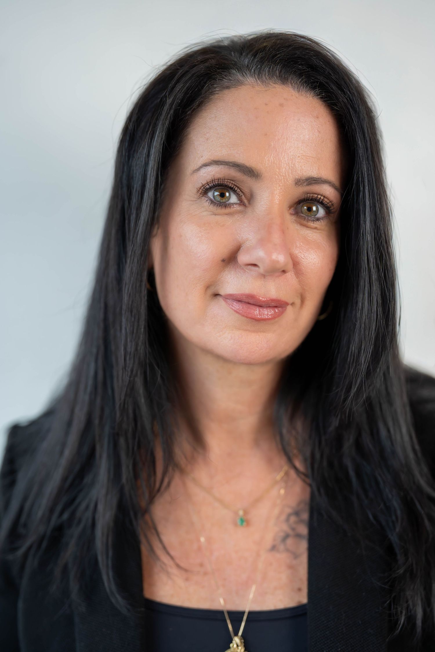 Professional headshot of a woman with long dark hair, wearing a black blazer and gold necklace.