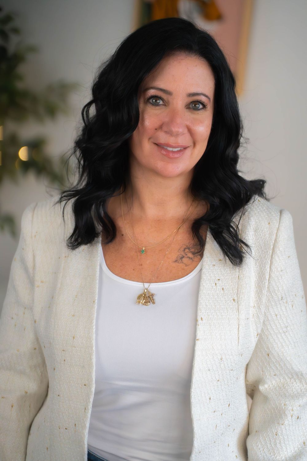 Professional portrait of woman in white tank top and cream cardigan with dark wavy hair.