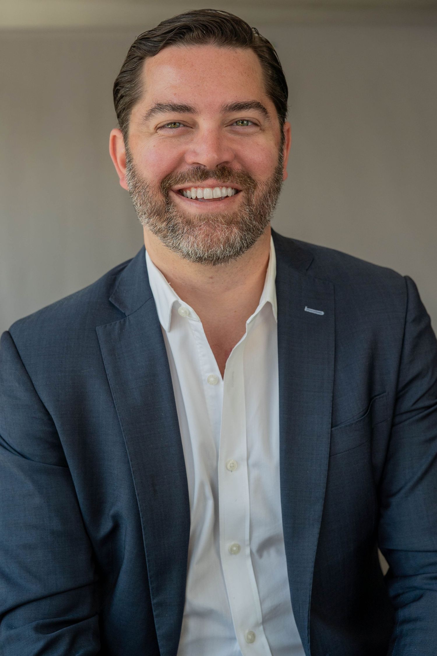 Smiling businessman with beard wearing navy blazer and white shirt in a professional headshot photo.