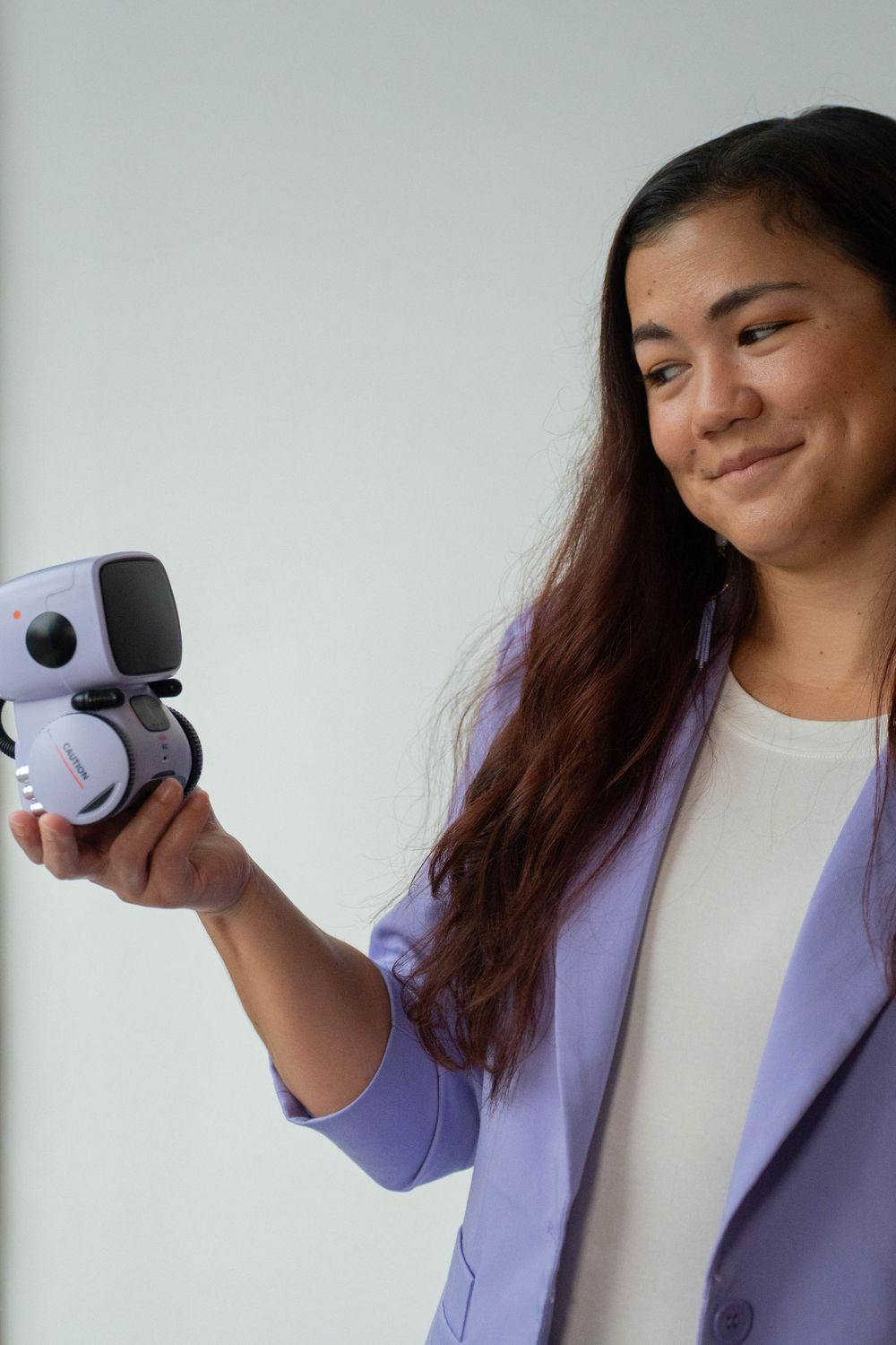 Person in purple blazer holding small robot or tech device against white background.