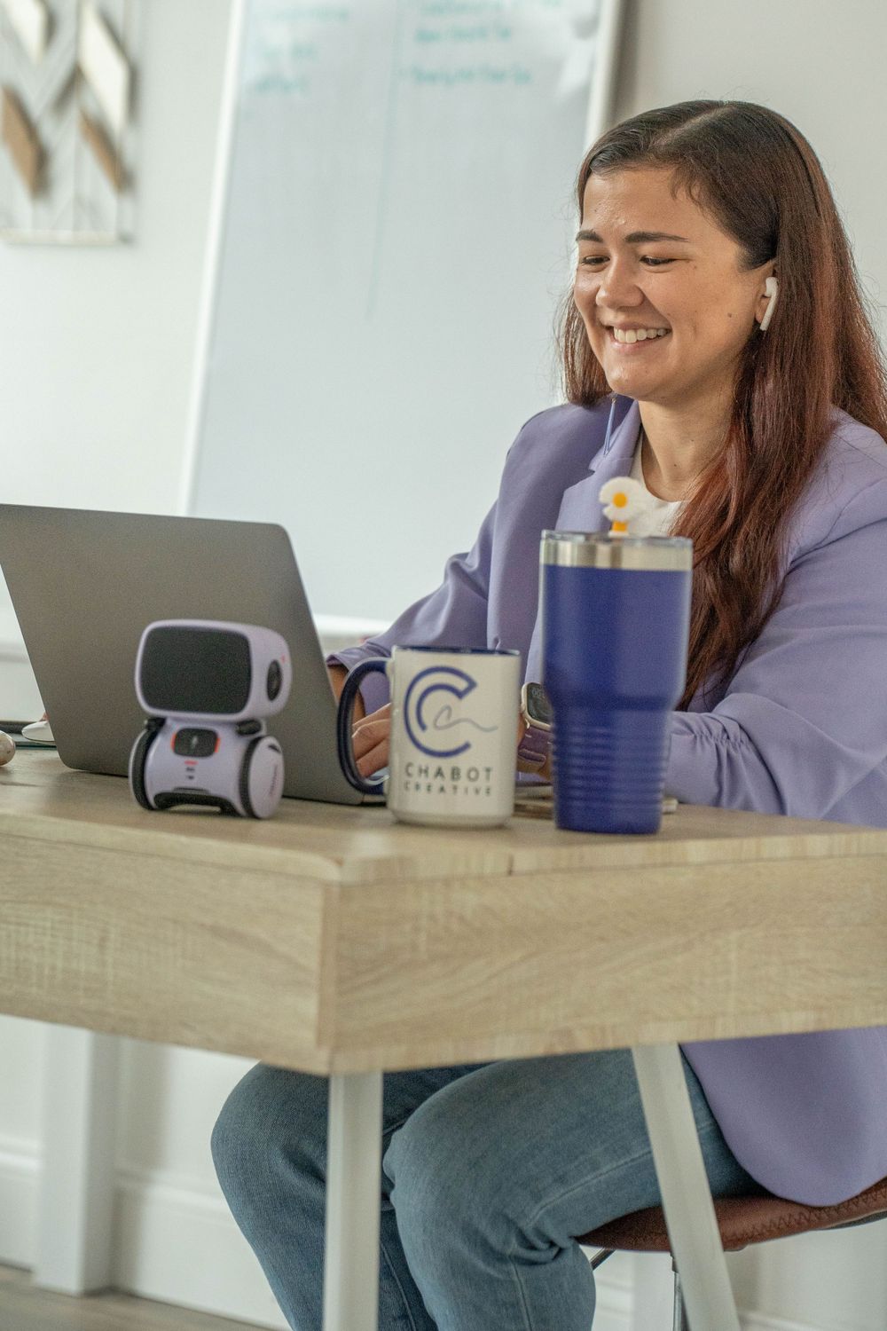 Remote worker at desk with laptop, robot companion, and branded coffee mug.