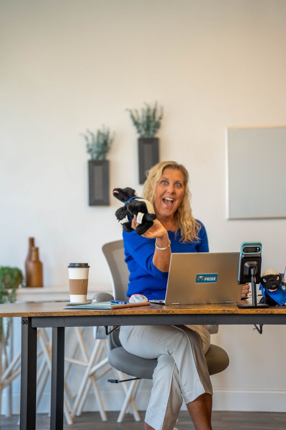 Person at desk with laptop showing excitement while holding small puppet or toy.