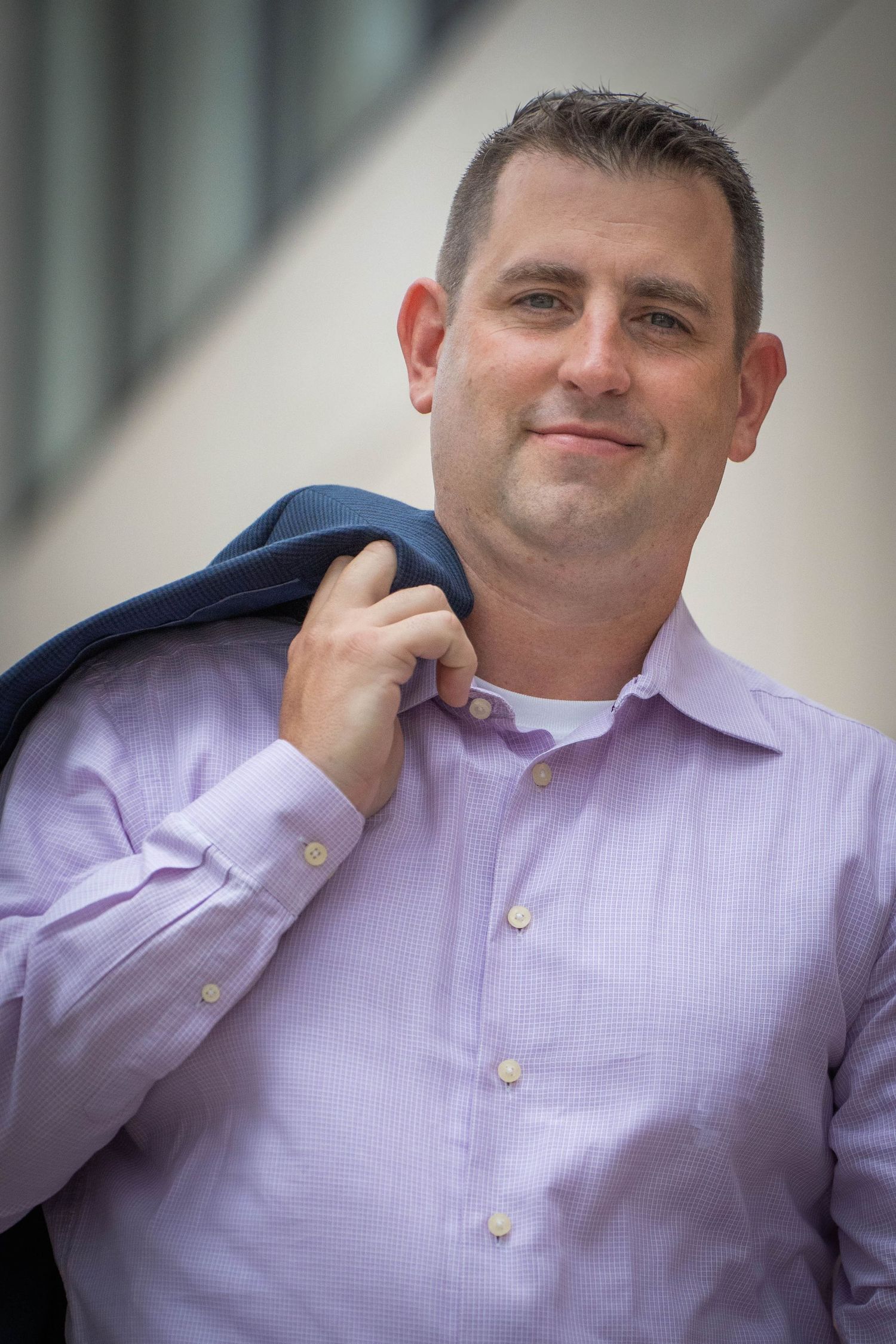 Professional headshot of person in light purple dress shirt against blurred background.