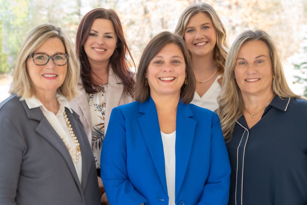 Group of five professional women in business attire posing together for team photo.