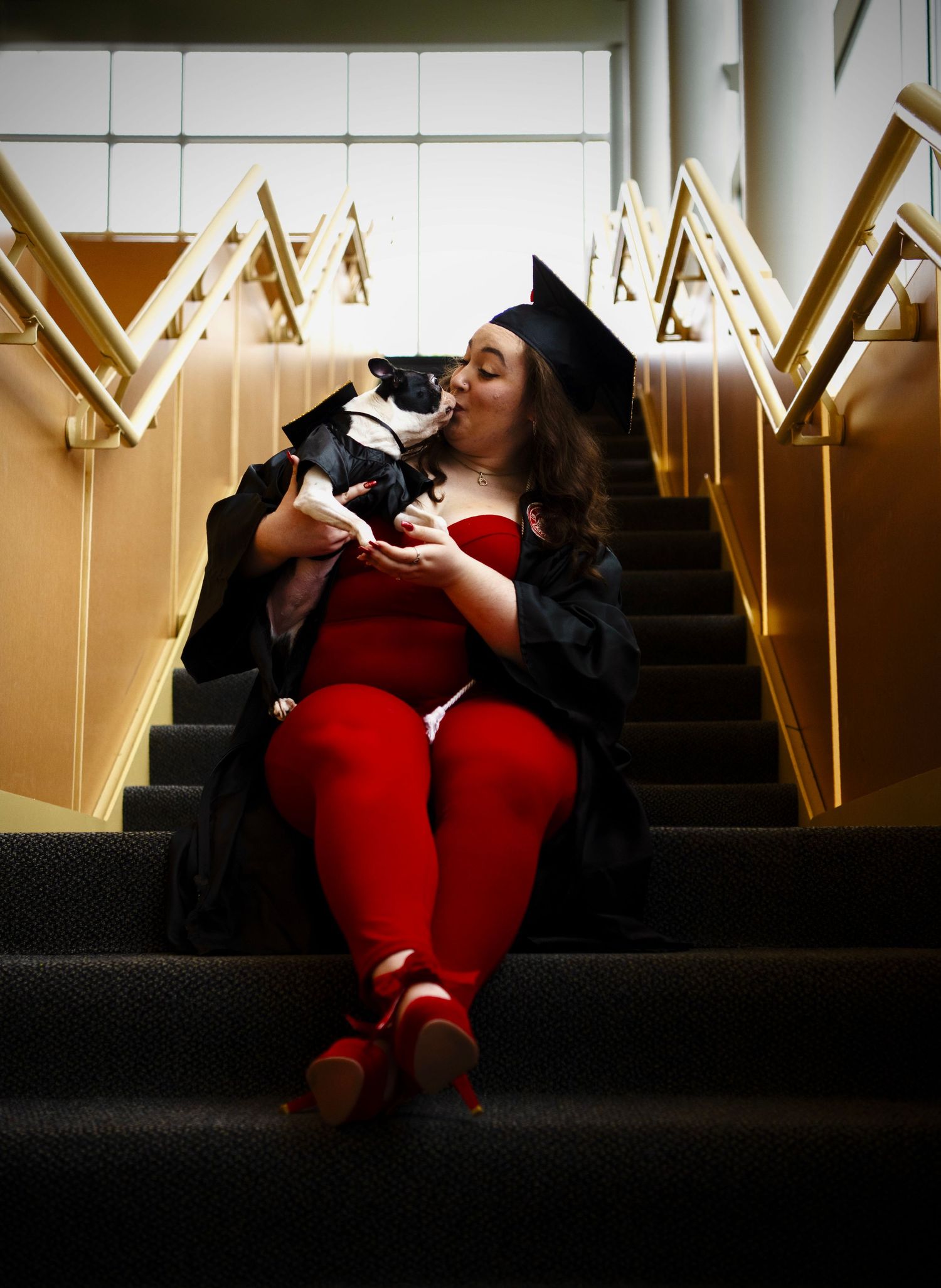 Bailey sitting on stairs in a cap and gown kissing her dog
