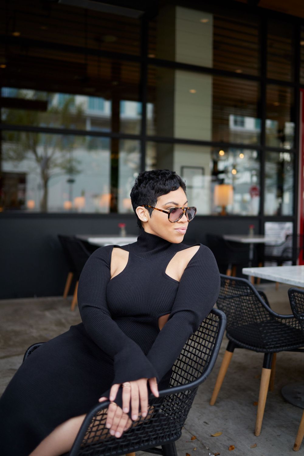 Person in black outfit relaxing on modern patio furniture with urban backdrop.