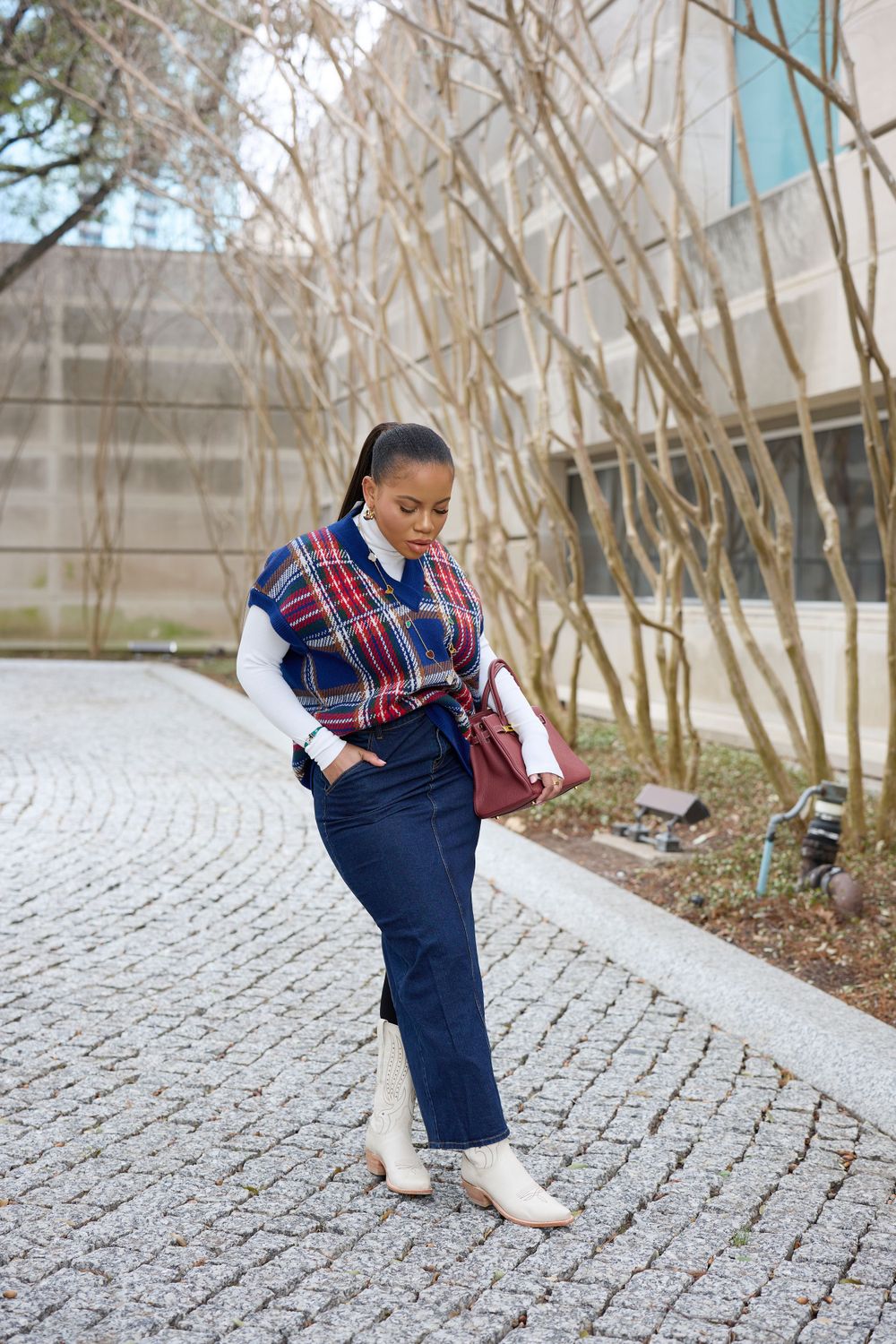 A casual winter outfit with plaid sweater and jeans on a cobblestone path.