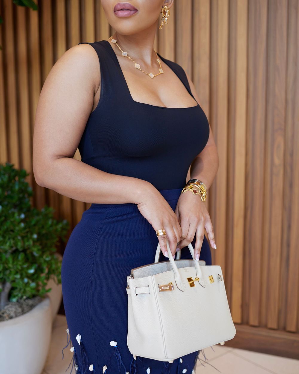 A sleek navy dress paired with a white designer handbag against wooden wall panels.