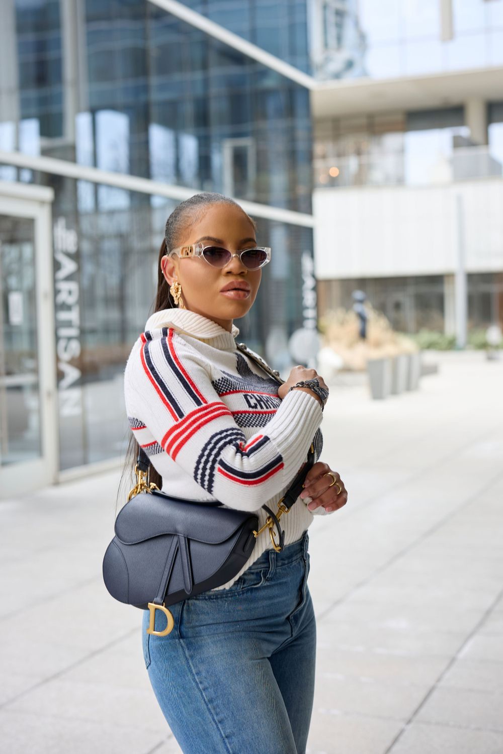 Person wearing casual sportswear outfit with white bomber jacket and blue denim jeans in urban setting.