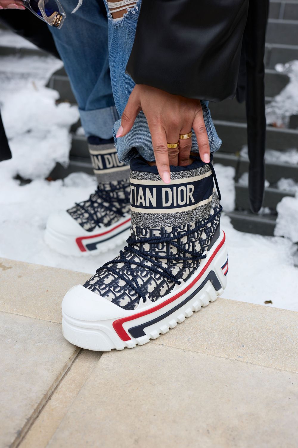Close-up of Christian Dior sneakers with navy, red and white design details on snowy ground.