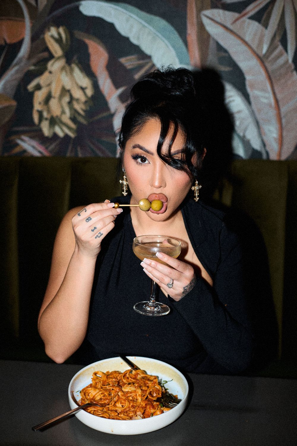 Candid dining scene with pasta dish and wine glass in dimly lit restaurant.