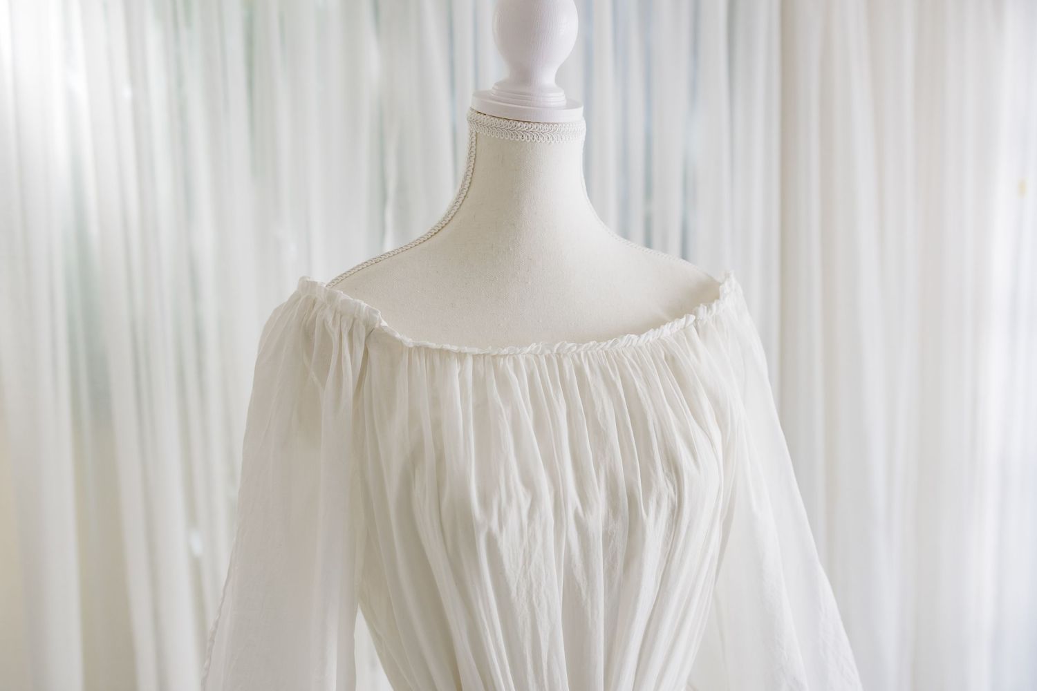 Off-shoulder neckline detail of white cotton dress showing gathered fabric and full sleeves.