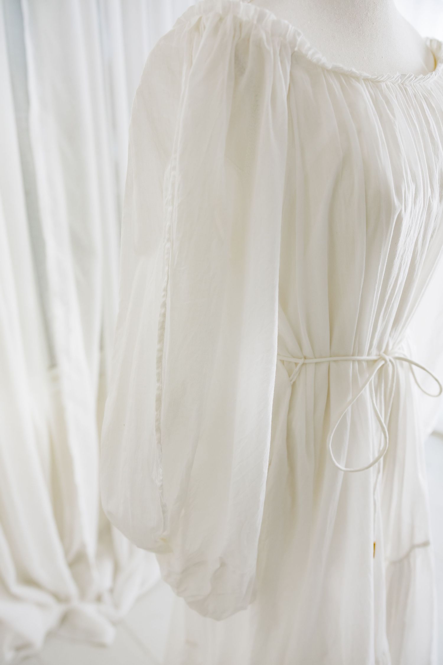 Side view of white dress showing flowing sleeve and delicate waist tie detail.
