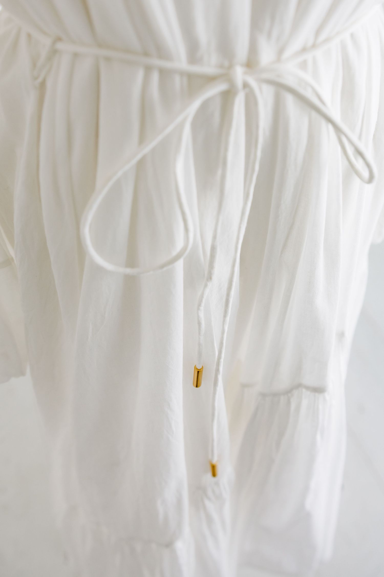 Close-up of thin white drawstring tie with gold bead accents on flowing dress.