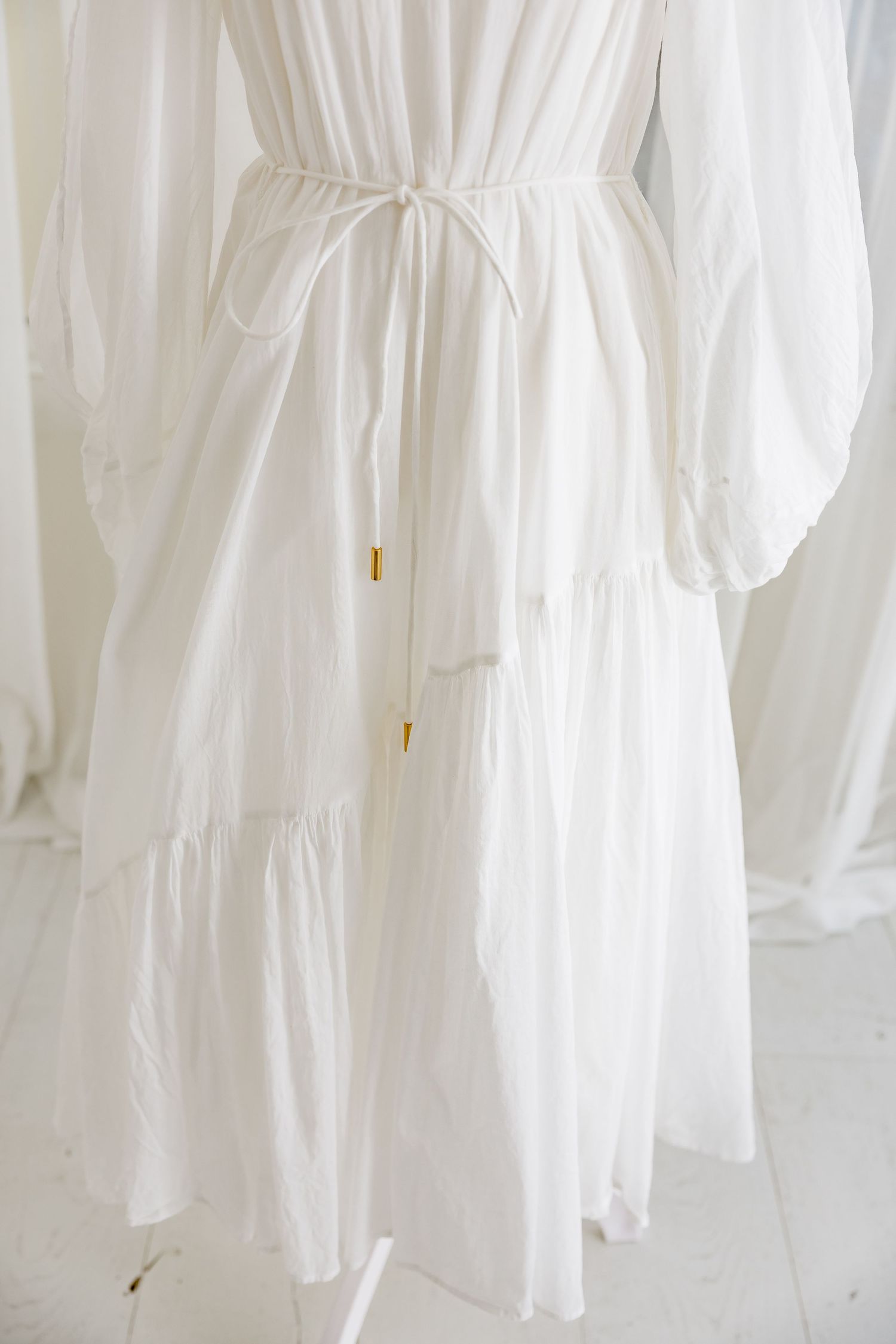 Flowing white maxi dress with cinched waist and tiered skirt shown against light background.