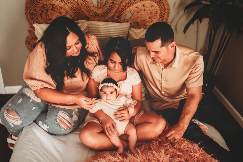 A family sits together on a bed with a baby, sharing an intimate moment in warm lighting.