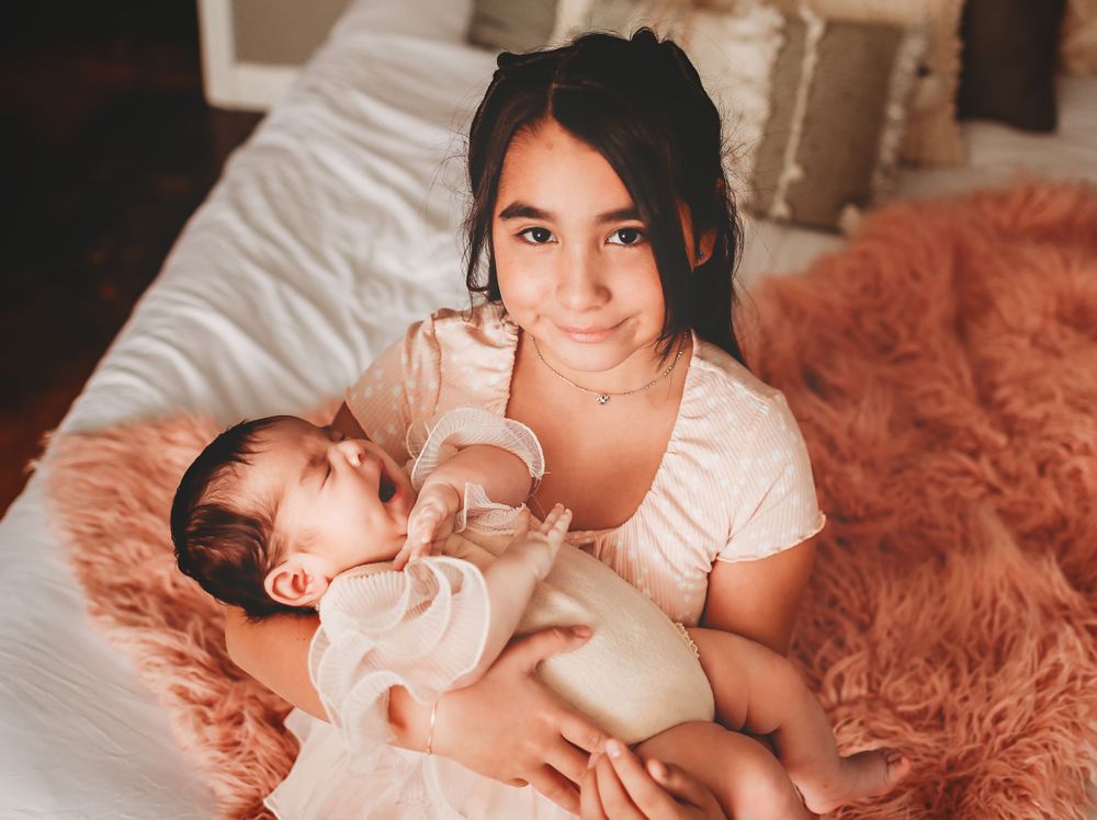 A tender moment between parent and newborn baby on a cozy bed with a rust-colored blanket.