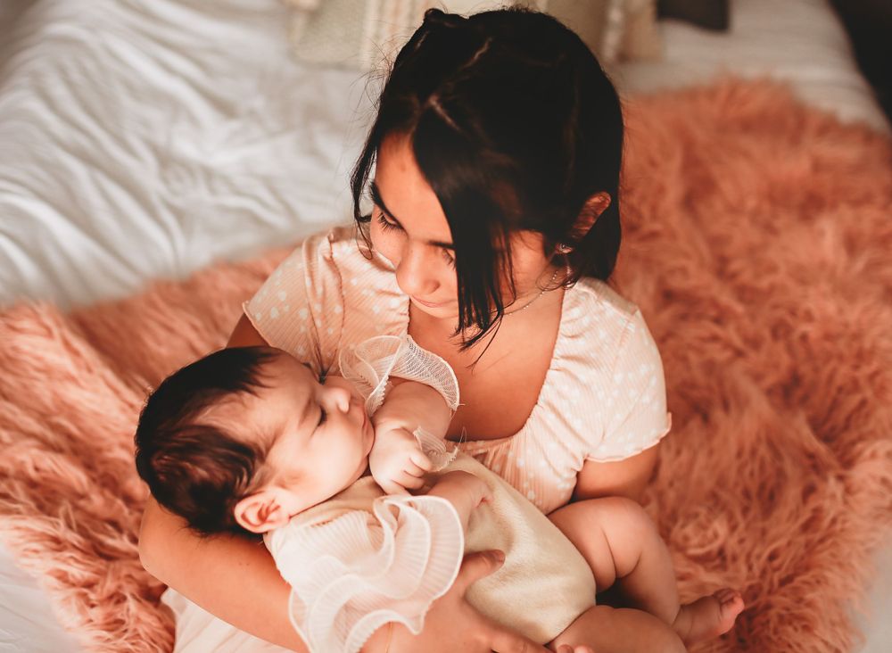 A tender moment captured on a plush rose-colored rug as a caregiver comforts a baby in soft natural lighting.