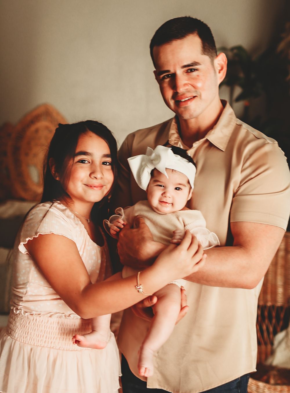 A family portrait showing three people in warm tones, with a baby wearing a white headband.