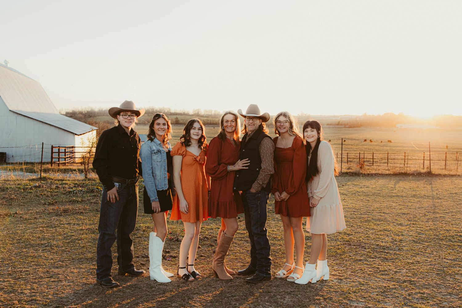 Group of people posing together at sunset in front of a rustic farm backdrop.