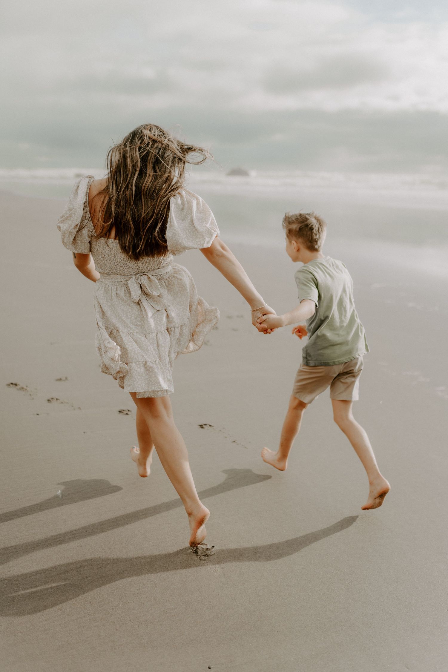 Two barefoot figures running joyfully together on a misty beach at sunset.