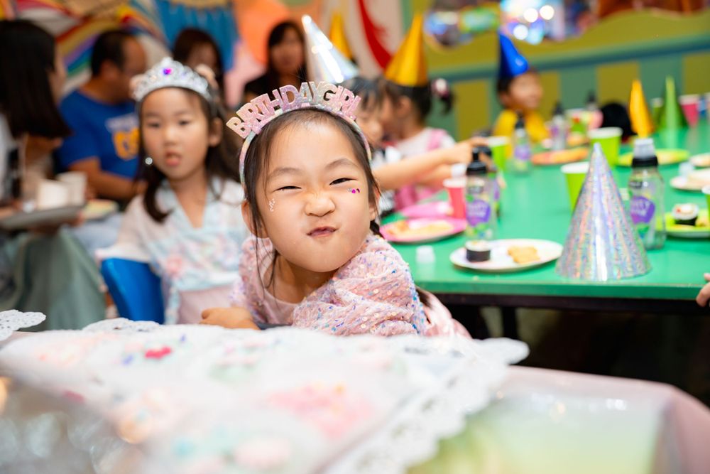 Joyful birthday girl blowing out candles with her best friends in a Rainbows End party room, by an Auckland event photographerJoyful birthda