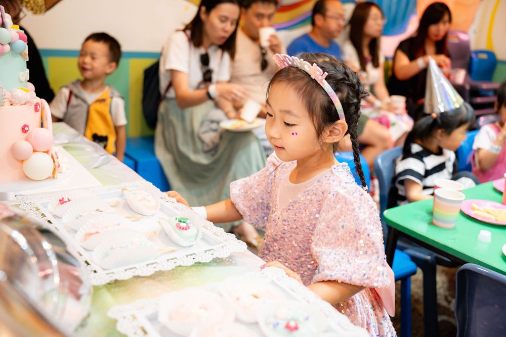 Joyful birthday girl blowing out candles with her best friends in a Rainbows End party room, by an Auckland event photographer.