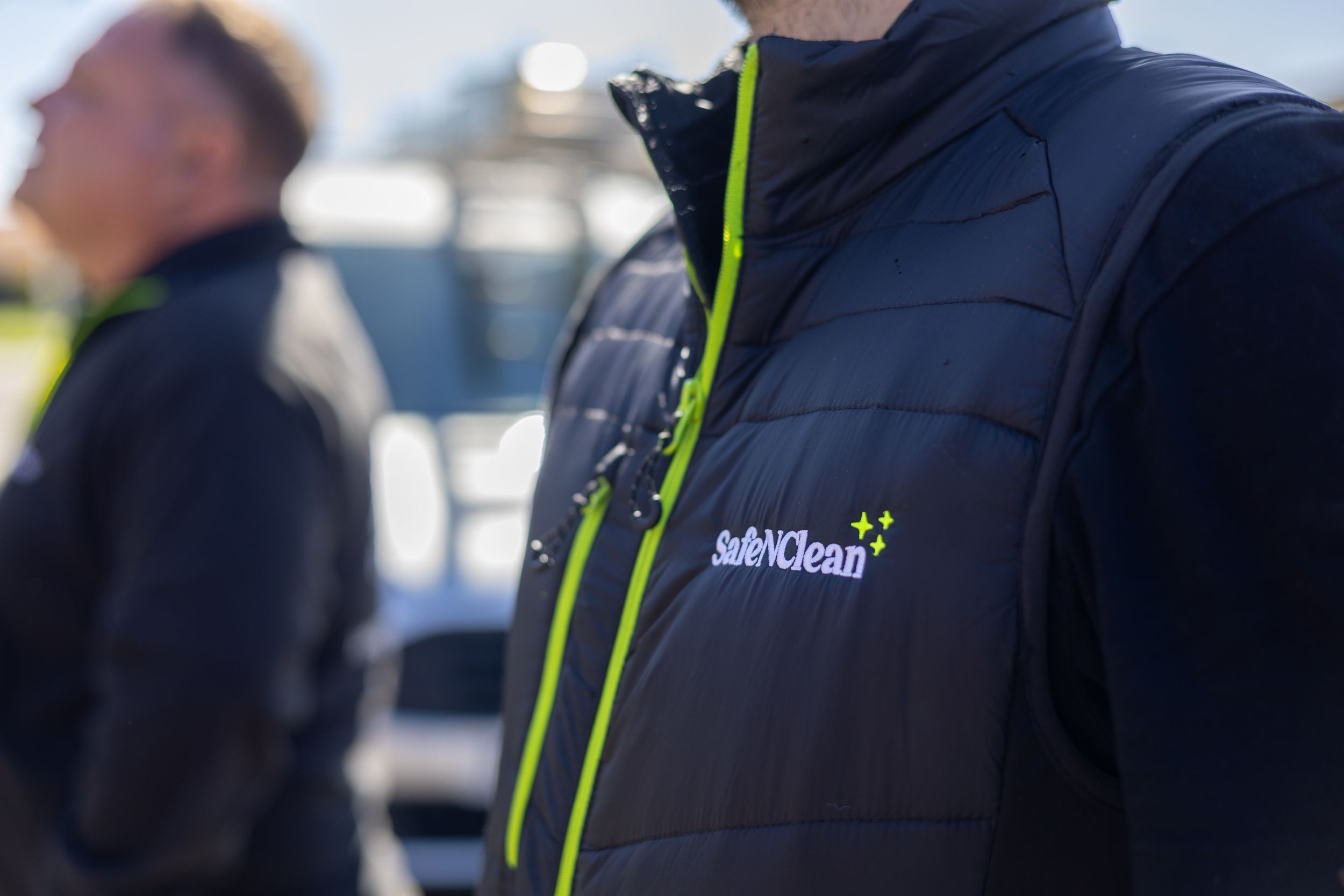 Close-up of a black puffy vest with lime green zipper trim and SafetyCulture company logo branding.