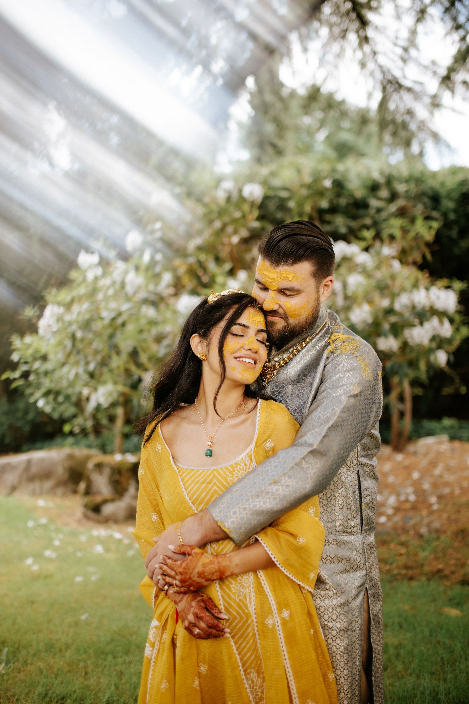 Romantic couple embrace in garden setting wearing yellow and silver traditional formal attire.