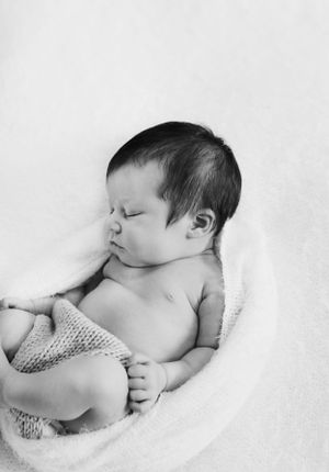 Sleeping newborn wrapped in knit blanket in black and white photograph.