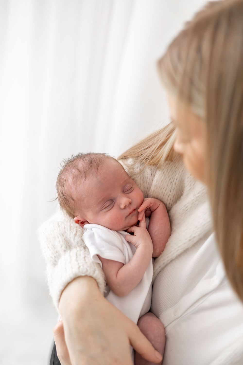 Newborn baby being cradled in soft white clothing against a light background during newborn shoot Nottingham