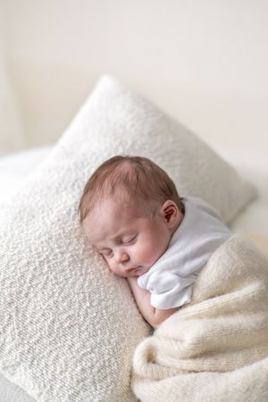 Natural baby photography Nottingham sleepy newborn wrapped in cream tones on a white pillow