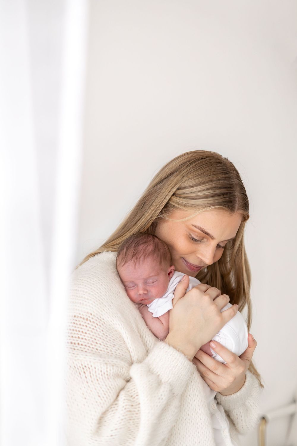 A tender moment captured in soft light as a mum in a cream sweater cradles her newborn baby, during newborn shoot Nottingham