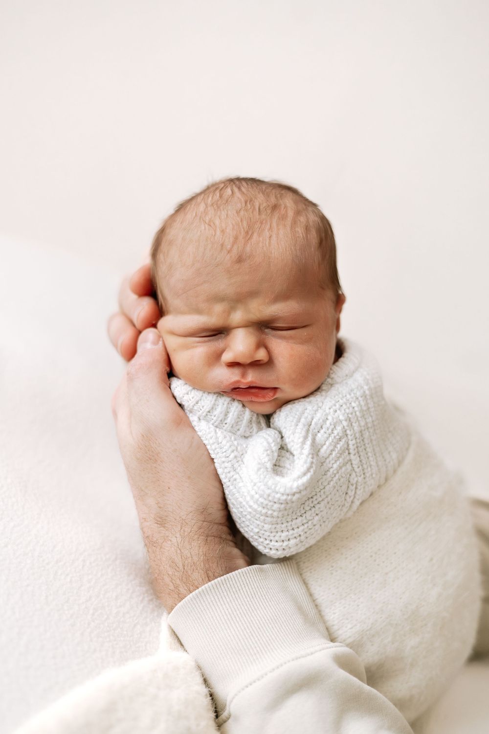 Baby photographer Nottingham newborn session baby in dads hands neutral styling cosy home studio