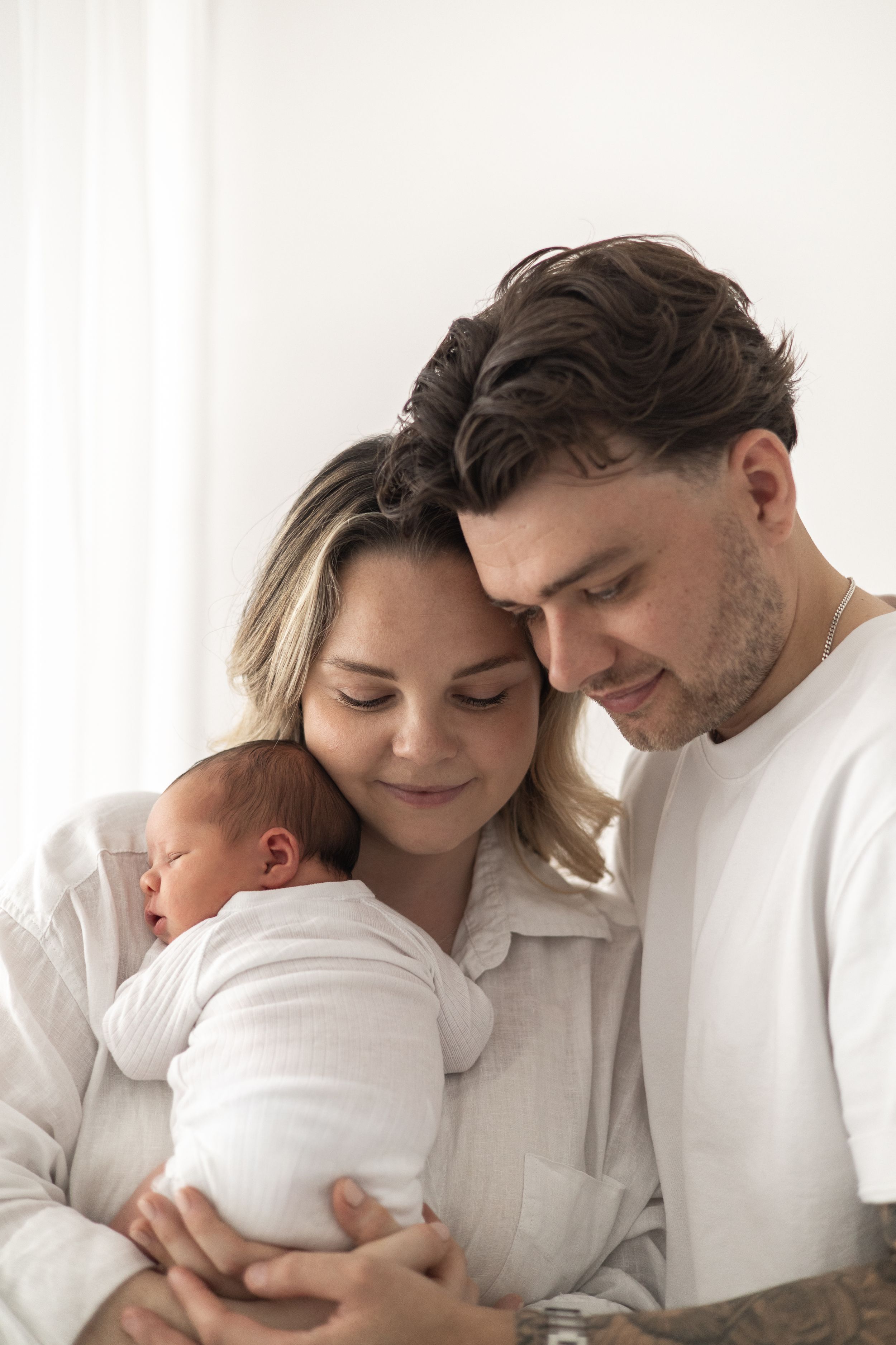 Mum and Dad tenderly holding their sleeping newborn baby, dressed in white nature newborn photographer Nottingham