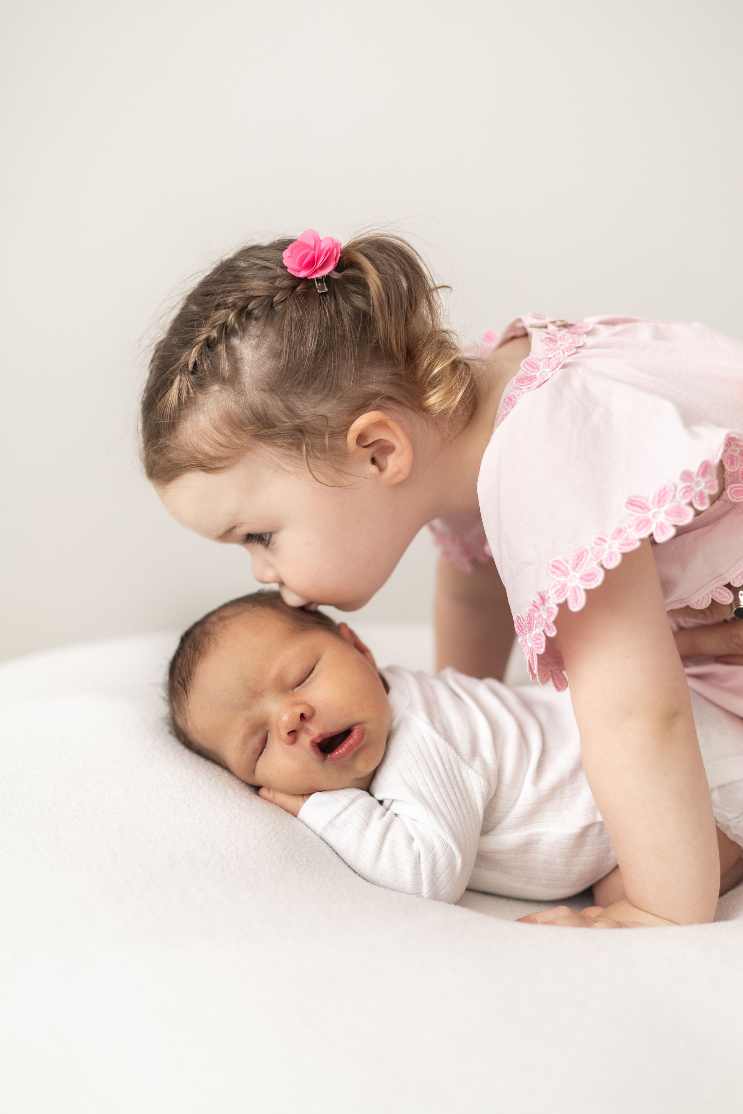 Young sibling gently kissing sleeping newborn baby on a white background nature newborn photographer Nottingham