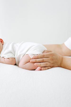 A gentle hand lovingly touches a baby's leg while lying on white bedding in a tender moment of care.